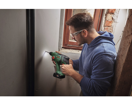 Un bărbat găurește un perete cu o mașină de găurit fără fir.