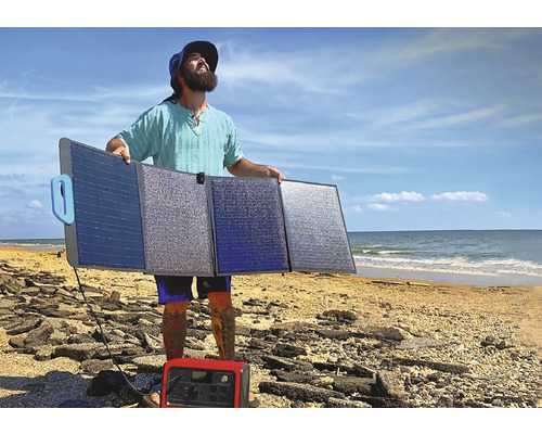 Bărbat ținând un modul solar pliabil pe plajă cu centrală electrică