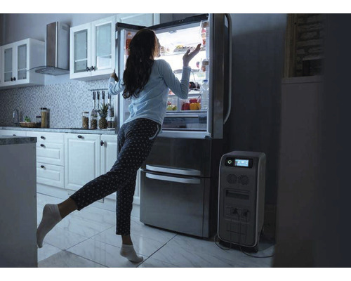 Femeie stând în fața unui frigider lângă un generator de curent într-o bucătărie.