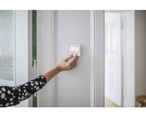 O persoană operează un termostat Bosch Smart Home pe un perete.