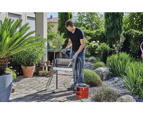 Bărbat curăță grătarul cu un aspirator de cenușă în grădină.