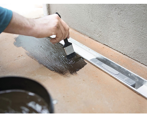 Aplicarea unei etanșări cu o pensulă pe o suprafață de podea cu jgheab de drenaj