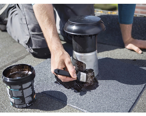 Un meșter etanșează o trecere de acoperiș cu bitum și o pensulă.