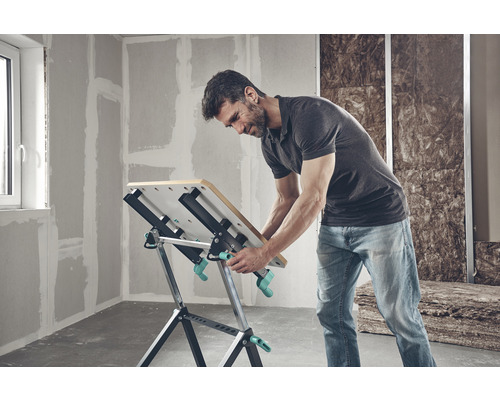 Un bărbat lucrează la un banc de lucru Wolfcraft într-o cameră nerenovată.