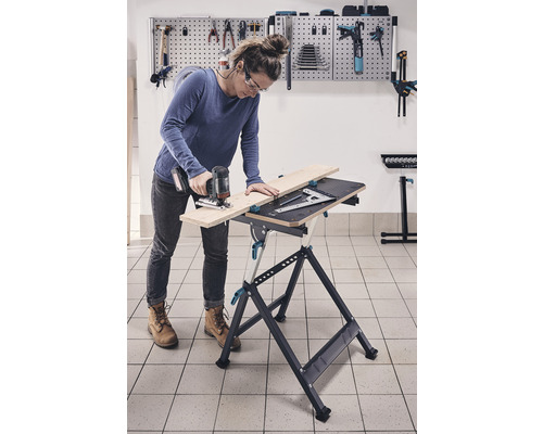 Femeie lucrând cu un ferăstrău vertical pe un banc de lucru într-un atelier.