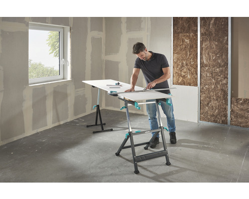 Un bărbat taie o placă de gips-carton pe o masă de lucru Wolfcraft într-o clădire în construcție.