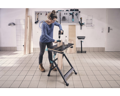 Femeie lucrând cu o mașină de găurit pe un banc de lucru într-un atelier.