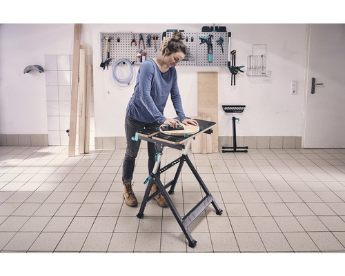 Femeie lucrând la un banc de lucru cu scule pe perete