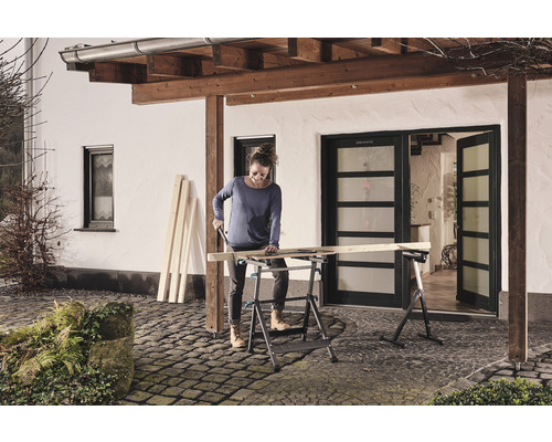 Femeie taie lemn pe un banc de lucru pliabil în aer liber.