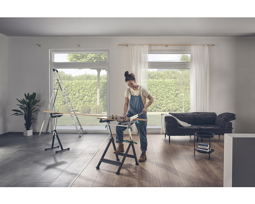 O femeie taie lemne pe un banc de lucru într-o cameră luminoasă