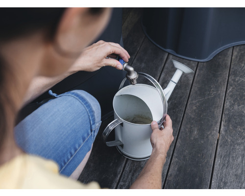 O persoană umple o stropitoare albă la robinet într-o grădină.