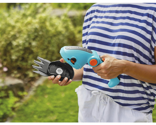 O persoană ține o foarfecă de iarbă fără fir Gardena cu cap de lamă interschimbabil.