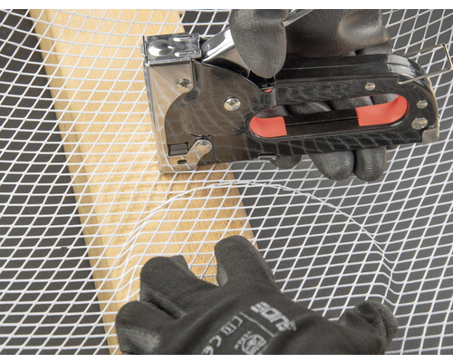 O persoană fixează plasă de sârmă pe un cadru de lemn cu un capsator.