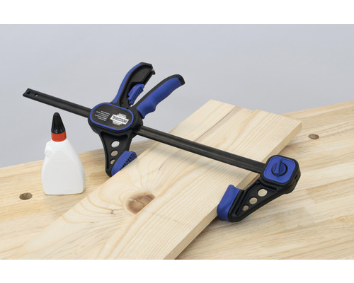 Clește cu bară fixează o scândură de lemn pe bancul de lucru lângă o sticlă cu adeziv pentru lemn