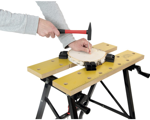 O persoană bate un cui cu un ciocan într-o bucată de lemn fixată cu un banc de lucru.