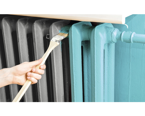 O persoană vopsește un radiator cu o pensulă.