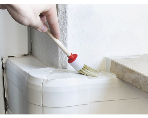 O persoană vopsește un colț cu o pensulă rotundă.