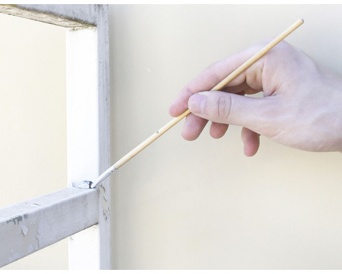 O mână vopsește cu o pensulă un grilaj metalic