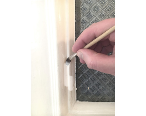 O pensulă este folosită pentru a aplica vopsea pe un cadru de fereastră.