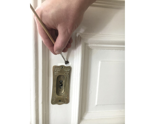 Vopsirea unei uși albe cu o pensulă lângă o gaură de cheie