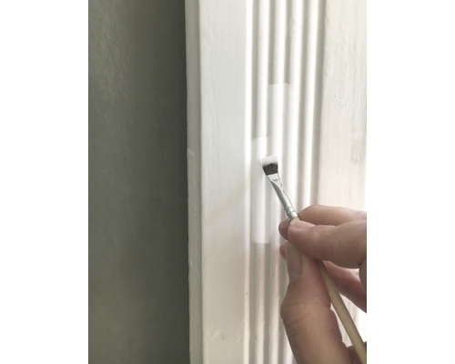 O persoană vopsește o bandă ornamentală albă cu o pensulă.