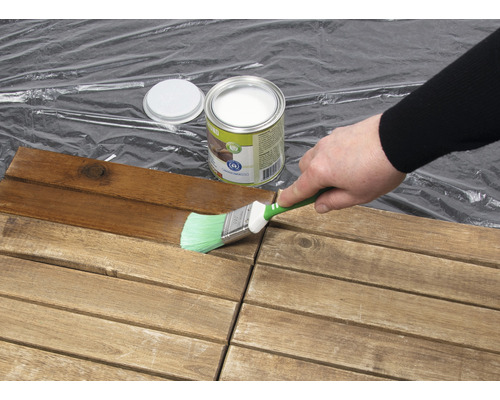 O persoană vopsește plăci de lemn cu o pensulă și lazură de protecție a lemnului.