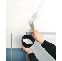 O persoană astupă o fisură în perete cu o spatulă. Se ține un vas cu material de umplere.