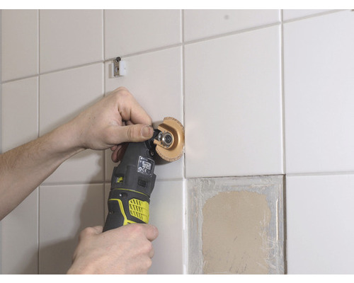 Unealtă electrică oscilantă care prelucrează un perete placat cu faianță.