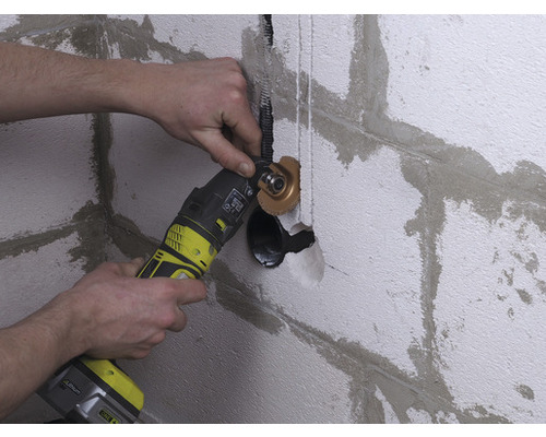 Un bărbat lucrează pe un perete cu un instrument multifuncțional pentru instalații sanitare