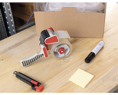 Scenă cu o cutie deschisă, folie cu bule, un derulator de bandă adezivă, un cutter, un marker și note pe o masă.