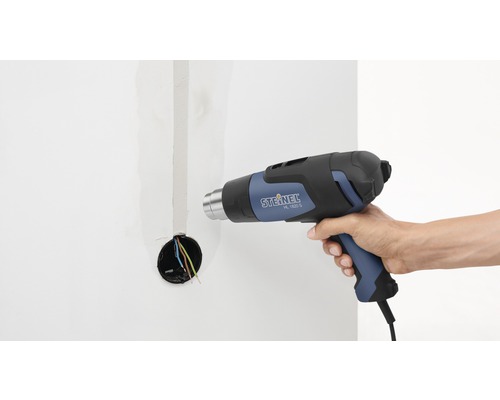 O persoană folosește un pistol cu aer cald Steinel, model HL 1620 S, pe un perete cu o cutie electrică