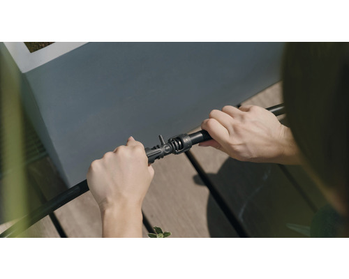 O persoană conectează un furtun de irigare la un conector.