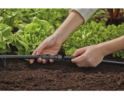 Persoană conectând un sistem de irigare într-o grădină