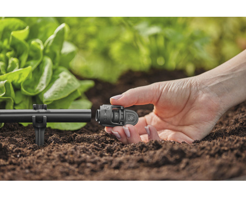 Prim-plan cu o persoană care fixează un conector la un sistem de irigație din grădină