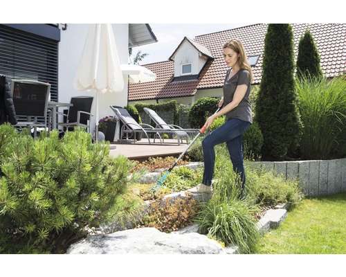 Femeie lucrează cu o greblă în grădină.