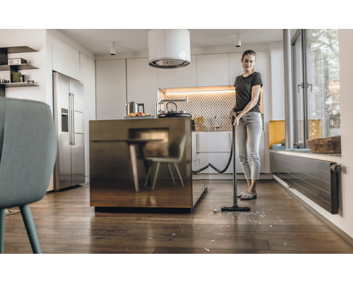 Femeie aspirând cioburi de sticlă cu aspiratorul în bucătărie