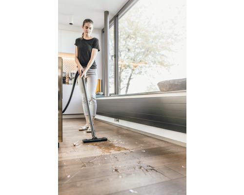 Femeie aspiră lichide și murdărie cu un aspirator umed-uscat de pe podeaua de lemn.