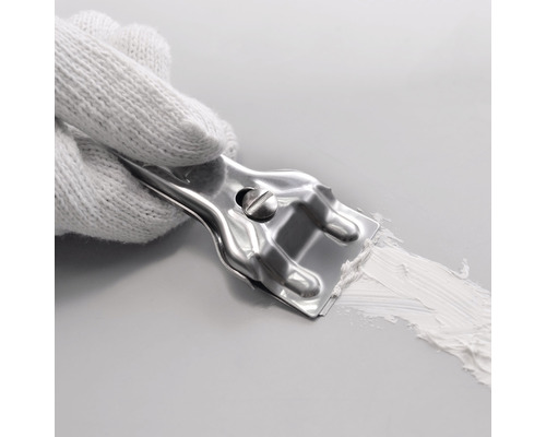 O mână cu o mănușă albă ține o spatulă metalică care aplică chit pe o suprafață.