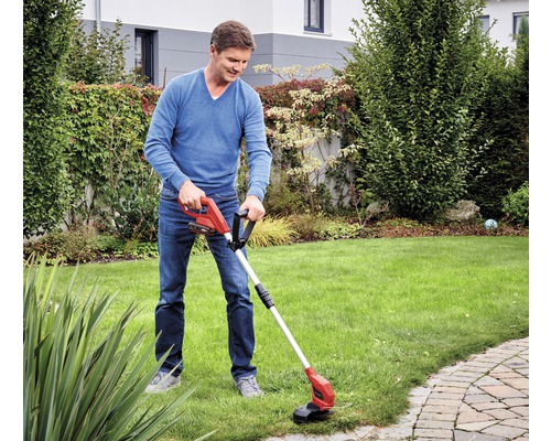 Un bărbat folosește o motocoasă cu acumulator în grădină.