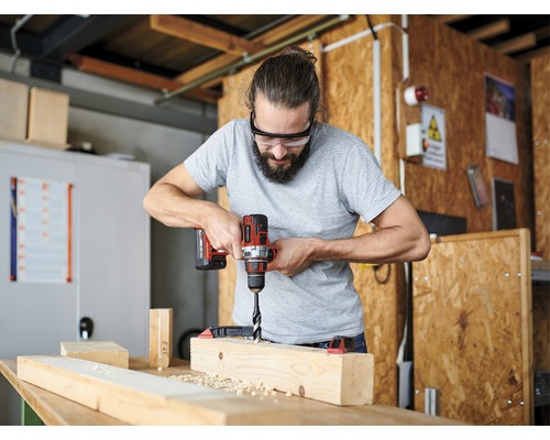 Un bărbat găurește o scândură de lemn cu o bormașină cu acumulator.