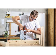 Un bărbat găurește cu o bormașină o scândură de lemn într-un atelier