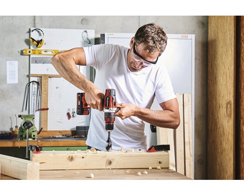 Un bărbat găurește cu o bormașină o scândură de lemn într-un atelier