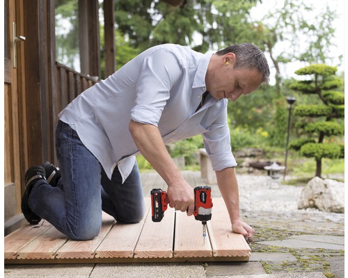 Bărbat îngenuncheat pe o terasă de lemn, lucrând cu o șurubelniță cu impact cu acumulator la fixarea scândurilor