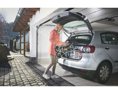 Femeie depozitează un cărucior de transport în portbagajul unei mașini într-un garaj.