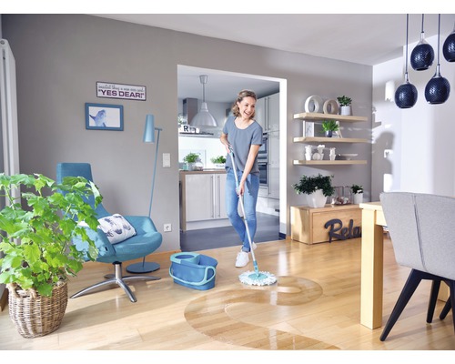 Femeie șterge podeaua de lemn într-un living luminos cu mopul