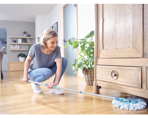 Femeie șterge podeaua de lemn din sufragerie cu mopul