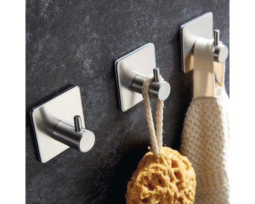 Trei cârlige autoadezive din oțel inoxidabil fixate pe un perete, cu un burete și un prosop pe ele.