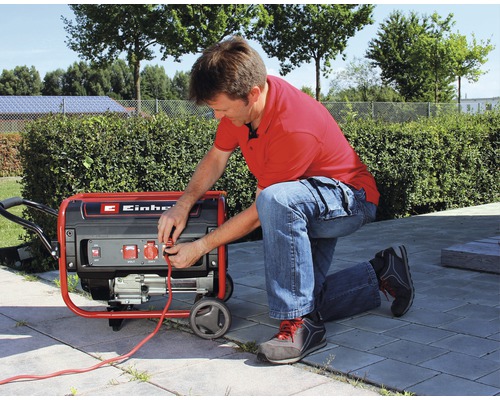 Un bărbat conectează un cablu la un generator de curent Einhell în aer liber.