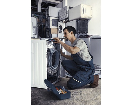 Un bărbat repară o mașină de spălat cu o cutie de scule