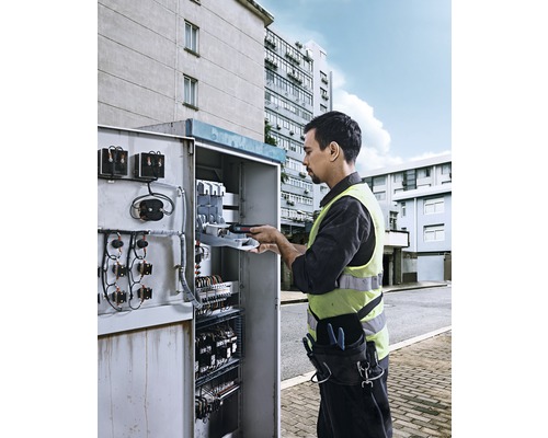 Electrician lucrează la o cutie de joncțiune deschisă în aer liber.